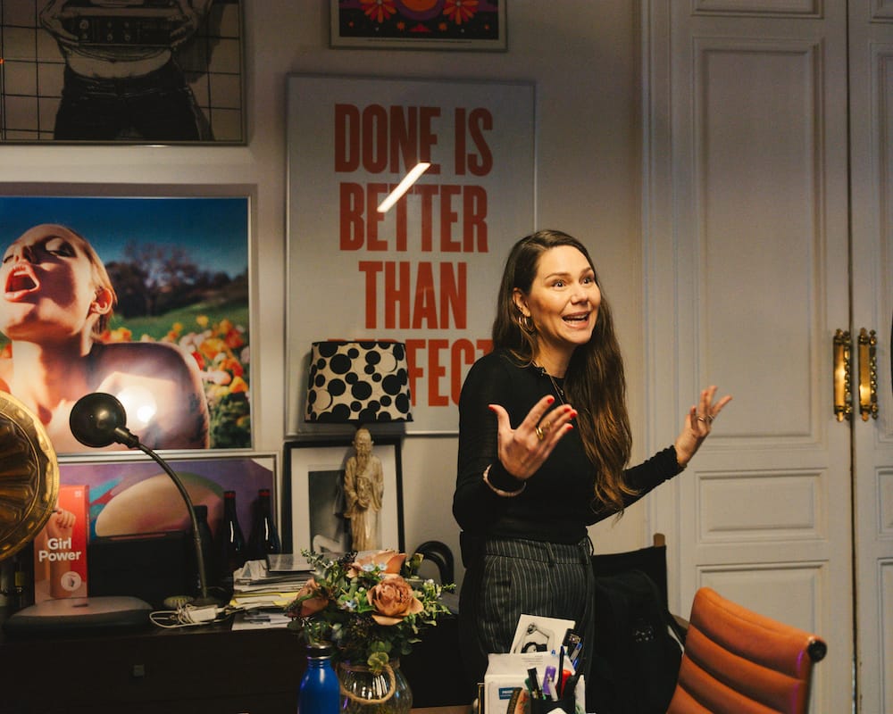 Erika Lust stands in a room cluttered with objects: a lamp shaped like a buddhist monk, a bunch of flowers, sheafs of paper.