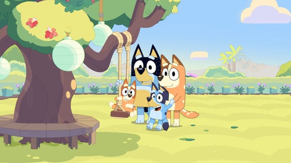 An animation still of the popular cartoon dog, Bluey, with her parents and sister by a tree.