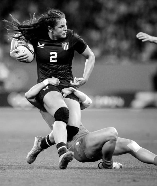 A black and white photograph of Ilona Maher being tackled by an opposing player in the Paris Olympics.