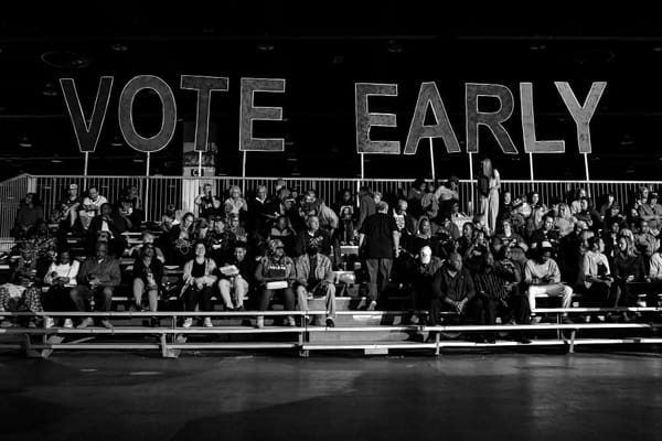 People sit on bleachers. Above them, giant letters spell out the words VOTE EARLY.