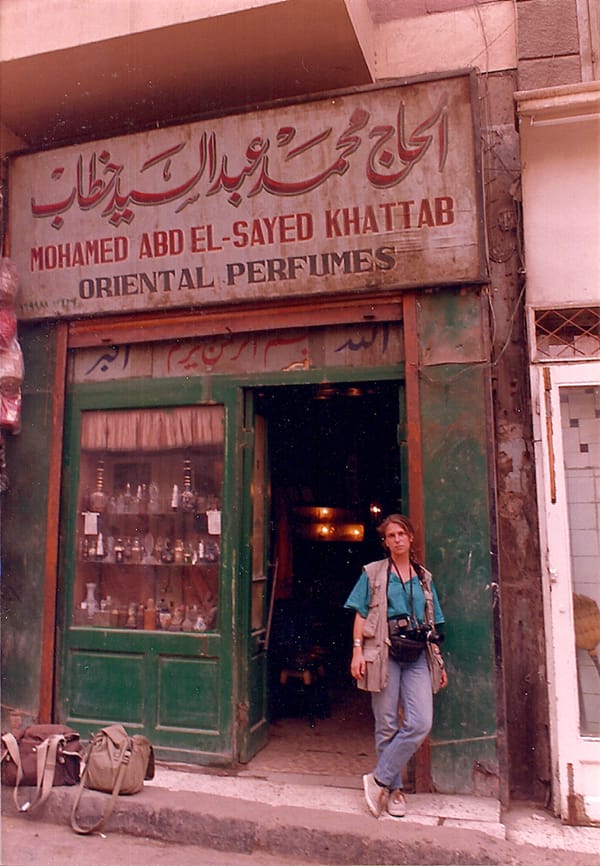 Deborah Copaken stands outside a store in Cairo in jeans and a utility jacket, with a camera around her neck.