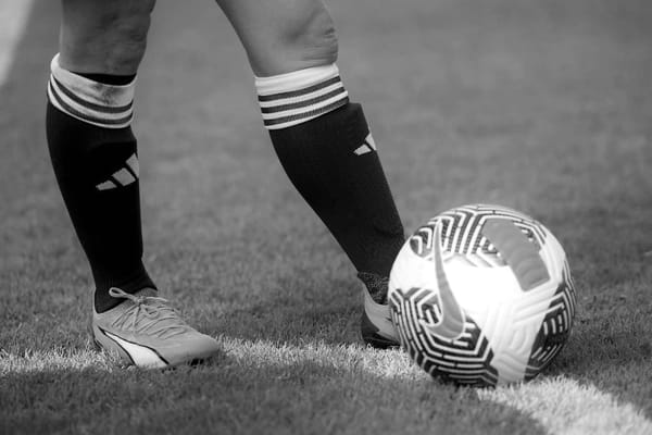 A photograph depicts a soccer player shown from the knees down, wearing cleats.