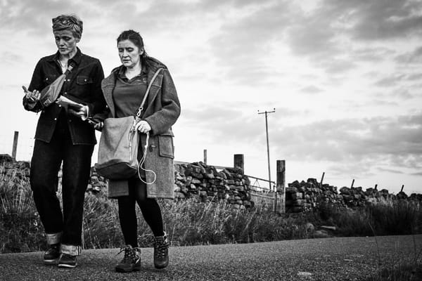 Black and white photo of Maxine Peake and Hayley Standing walking down a lane in Yorkshire. Behind them is a dry-stone wall.