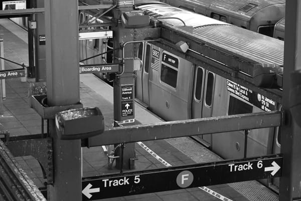 Black and white photo of a New York subway platform, where a train waits with closed doors.